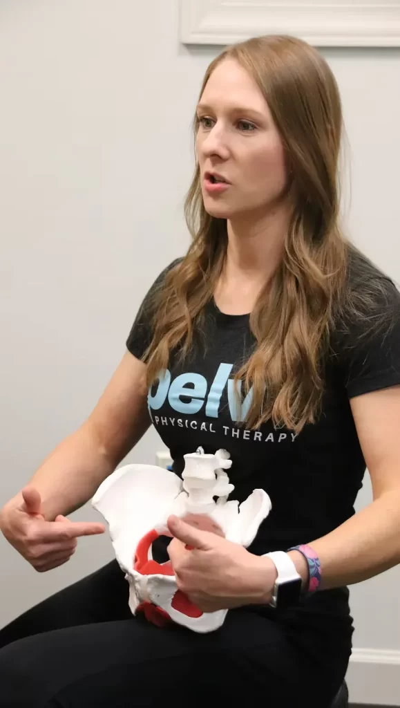 A person wearing a "pelvRX" shirt holds a pelvic bone model, emphasizing a point with their fingers. The scene conveys an educational tone.