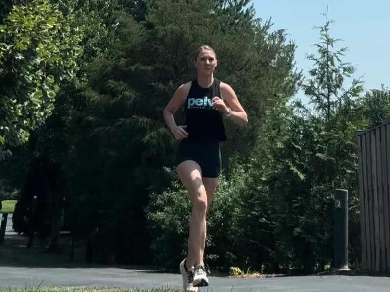 A person in athletic gear jogs on a sunny day, surrounded by lush greenery and trees, conveying a sense of determination and focus.